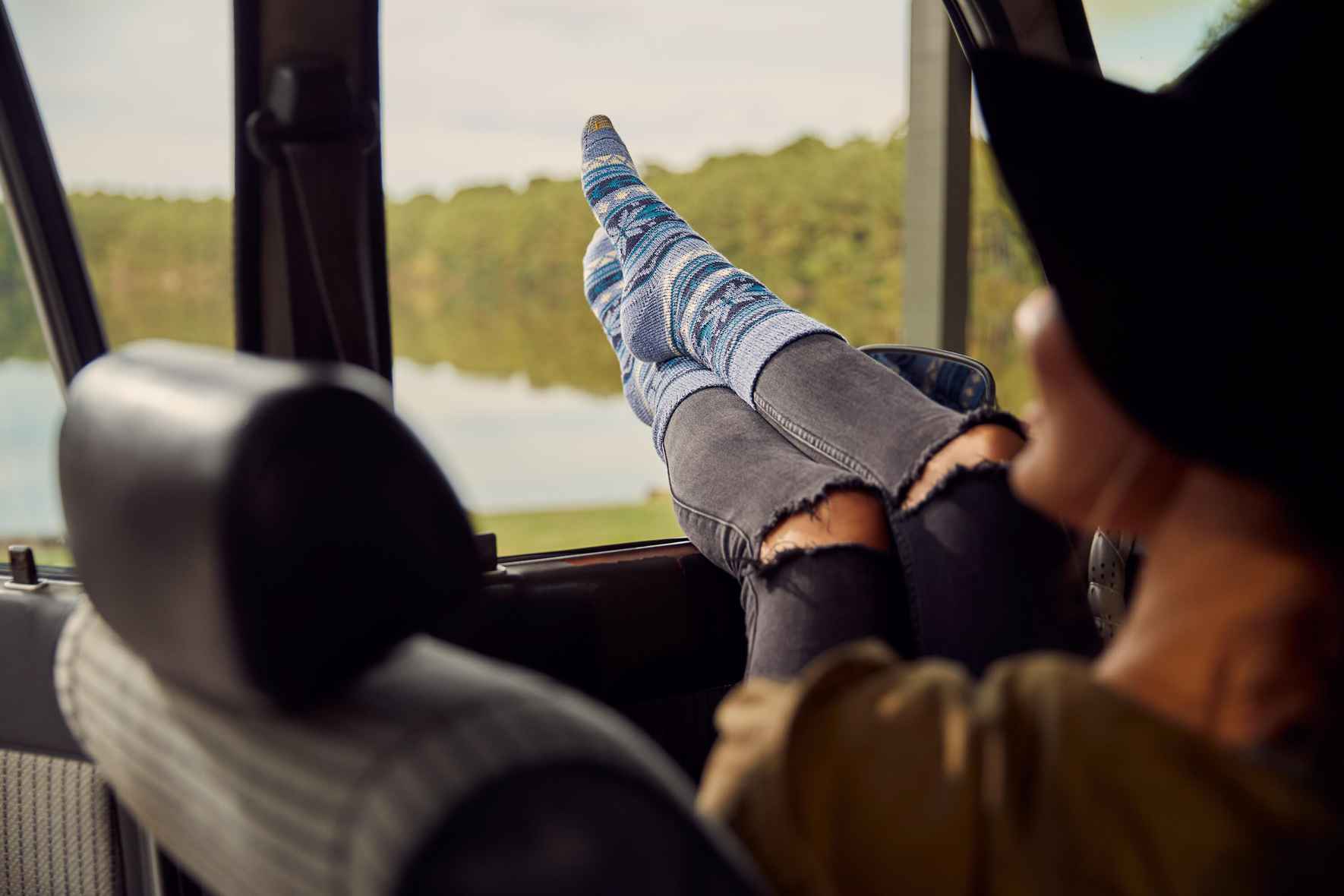 A woman with blue socks has her feet out the car window with the GOLDTOE™ logo in the center.