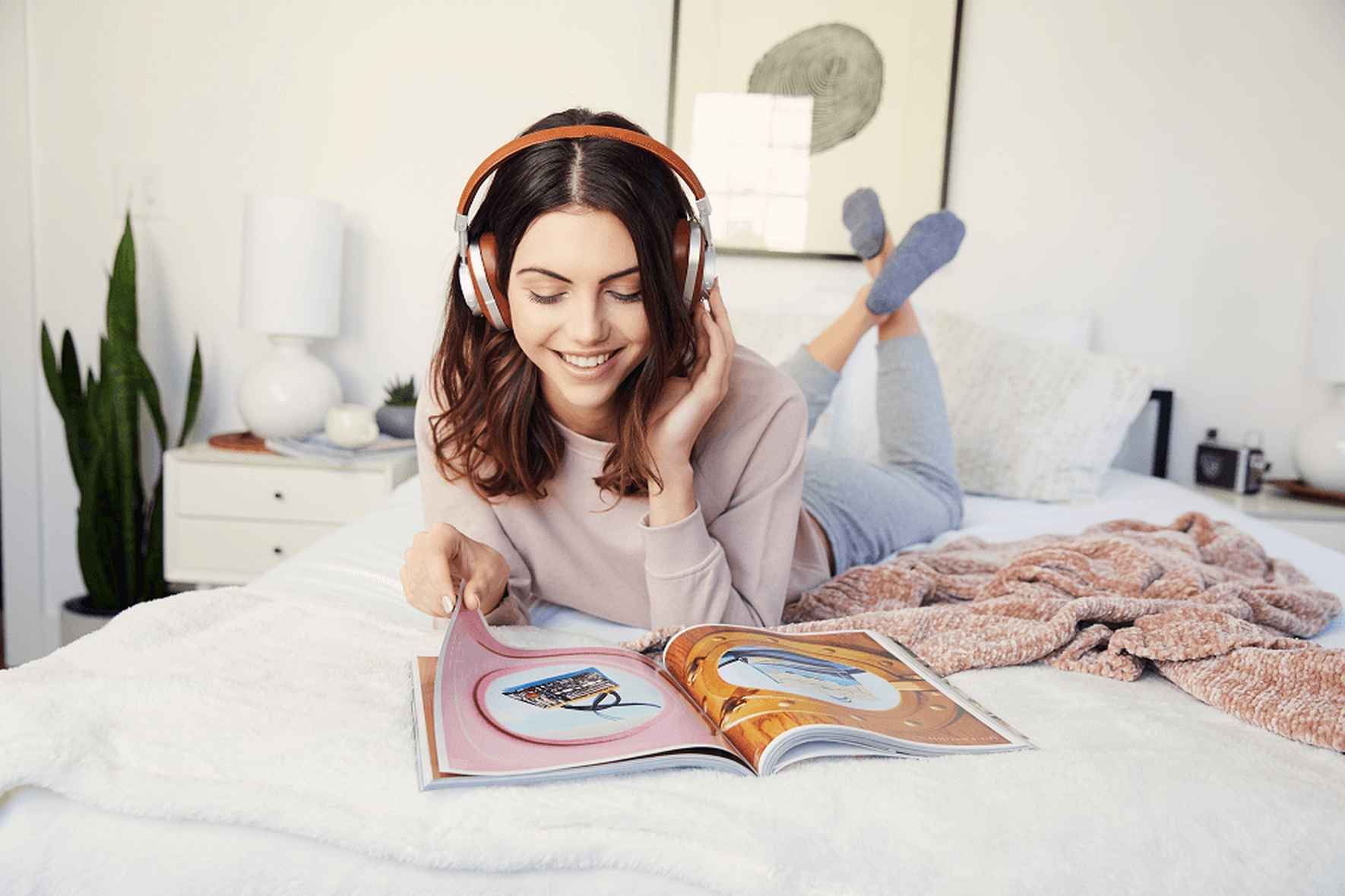 Una mujer con audífonos está en su cama leyendo una revista con el logo de Peds™ en el centro.
