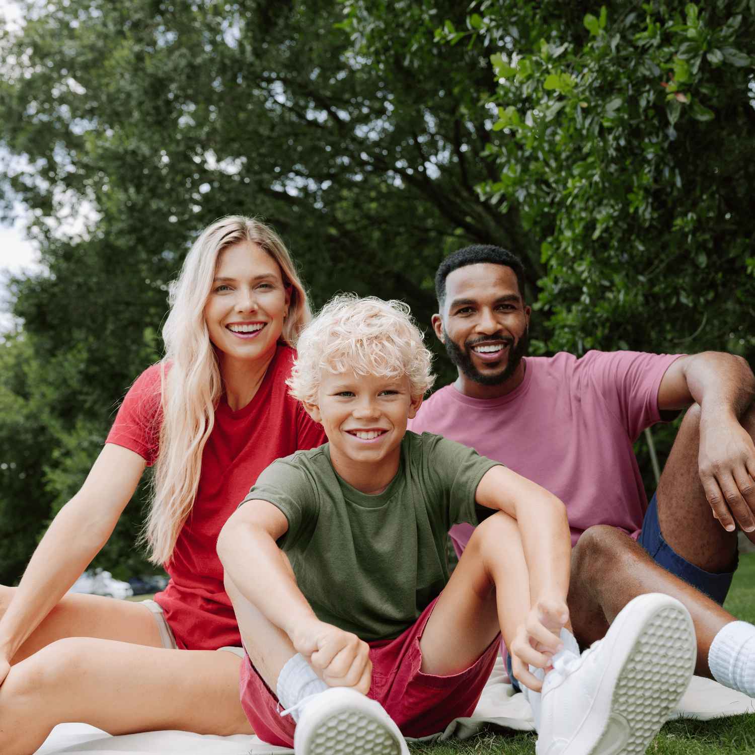 Une femme, un homme et un garçon sont assis sur l'herbe et sourient.