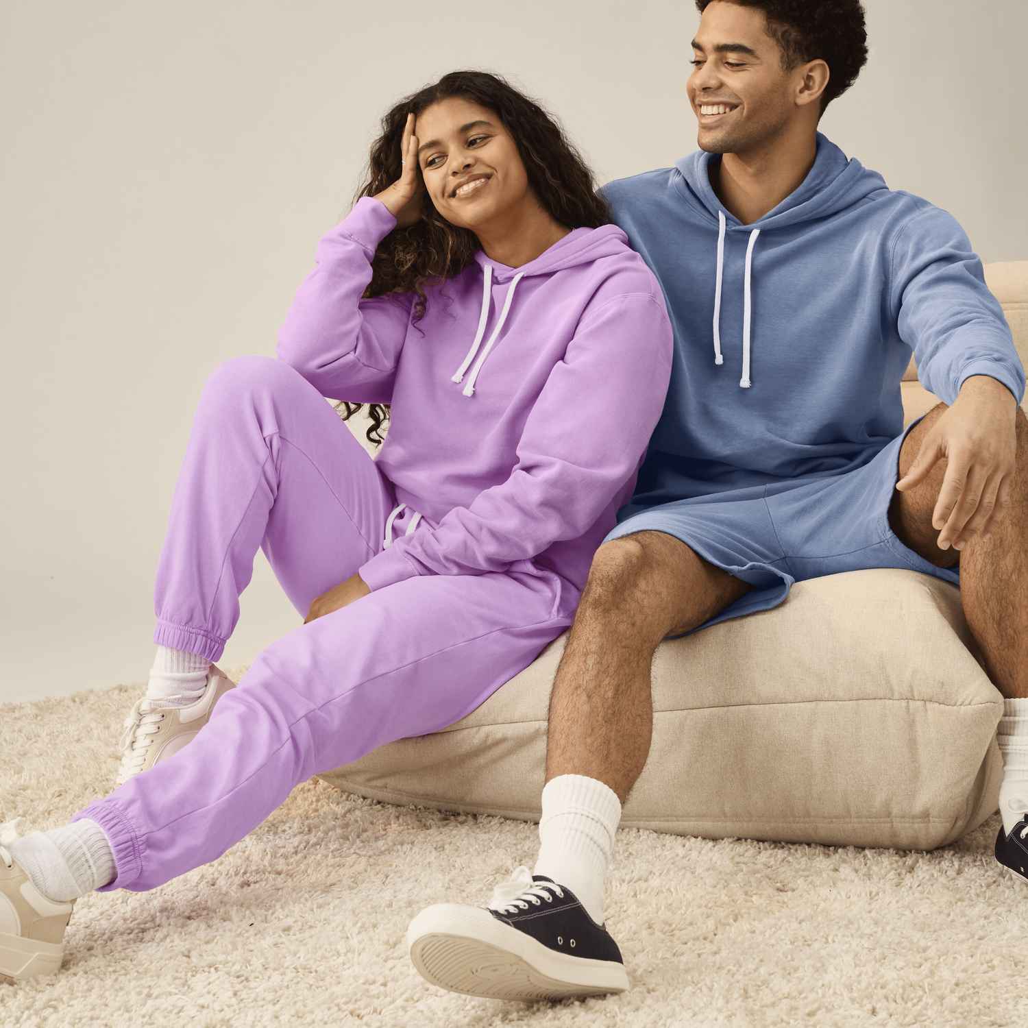 Une femme et un homme portant un survêtement Comfort Colors violet et bleu sourient sur un canapé.