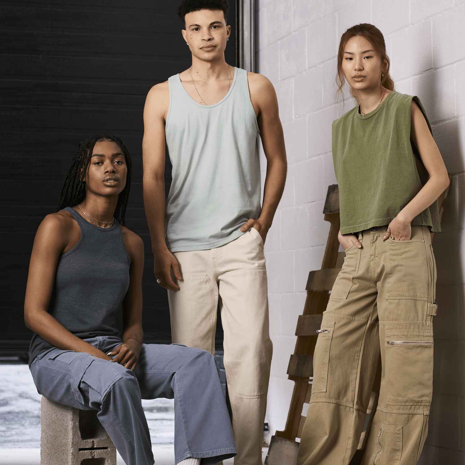 Deux femmes et un homme portent des débardeurs American Apparel et regardent la caméra dans un environnement industriel.