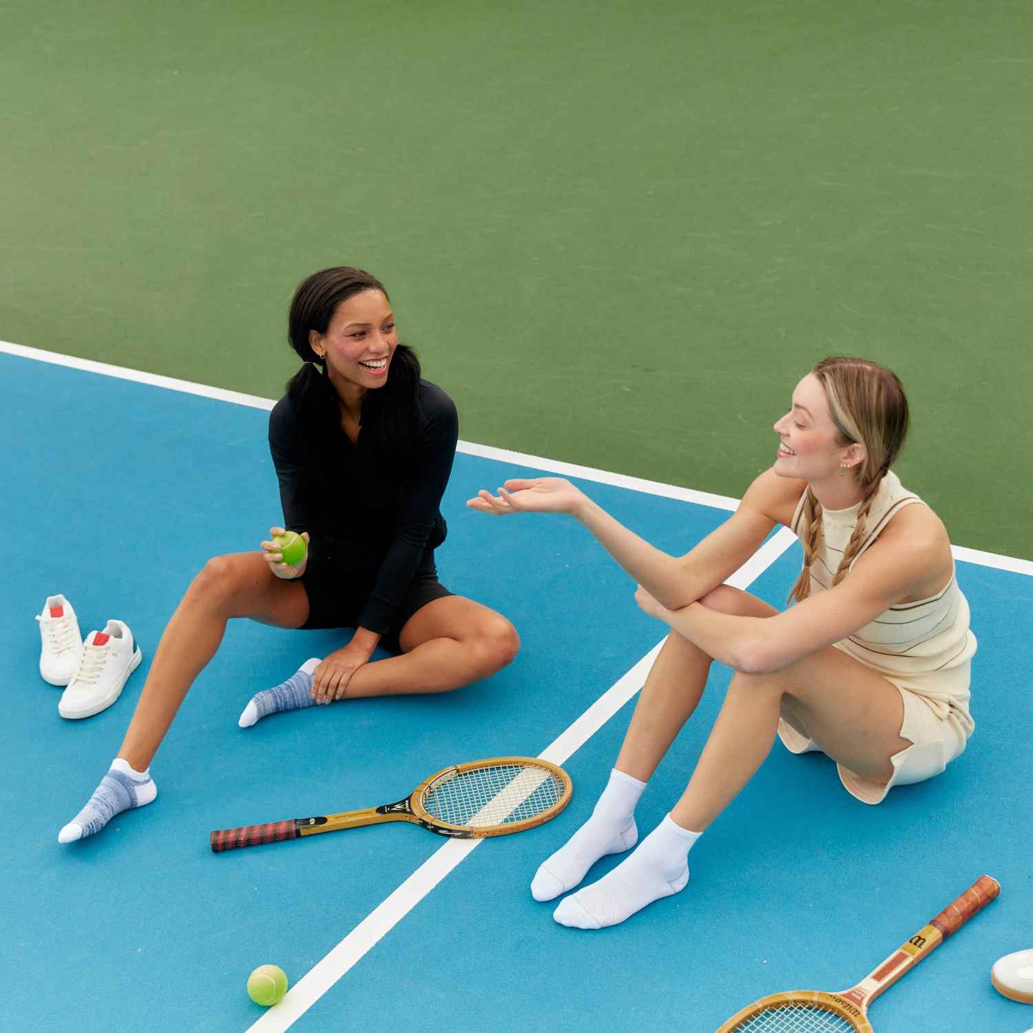 Deux femmes sont assises sur un court de tennis dans leurs chaussettes Peds, discutant et souriant.