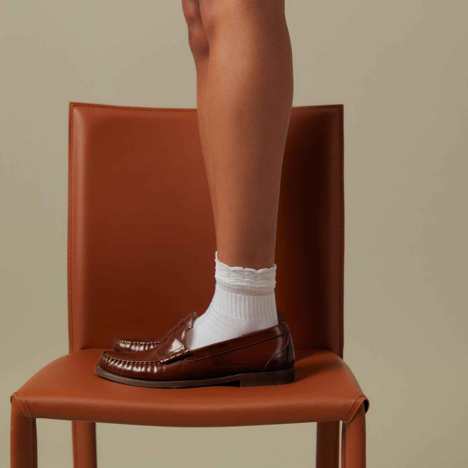 Une femme est debout sur une chaise en cuir marron et porte des chaussettes Peds blanches.