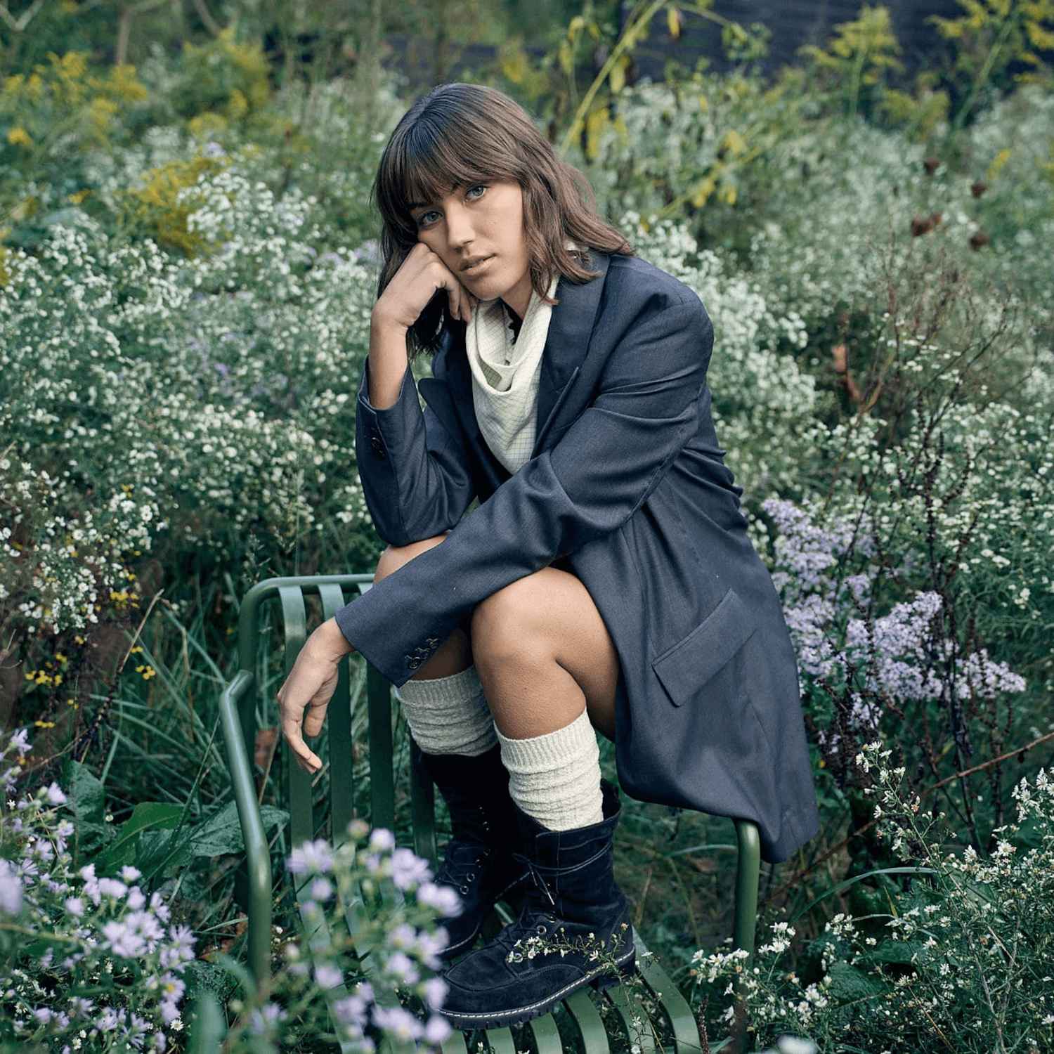 Une femme est assise sur une chaise dans un champ de fleurs et porte des chaussettes hautes blanches GOLDTOE.