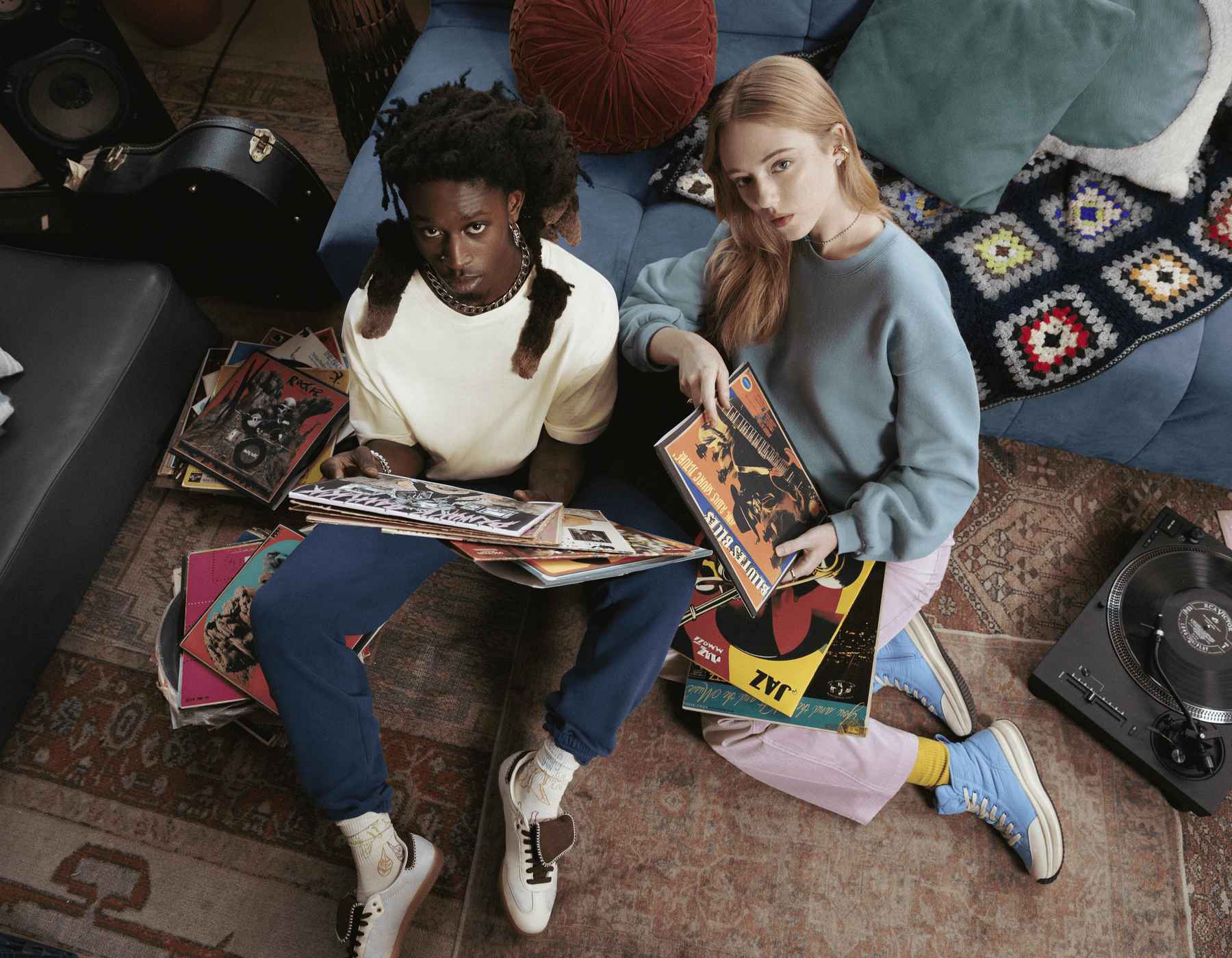 Un homme et une femme sont assis par terre et regardent la caméra en tenant des disques vinyles.