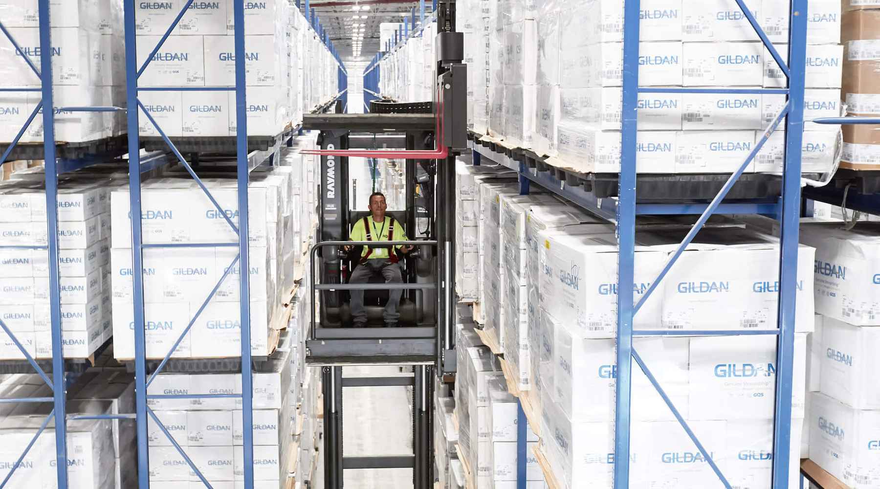 A Gildan employee at our distribution centre is operating a forklift between stacks of Gildan boxes.
