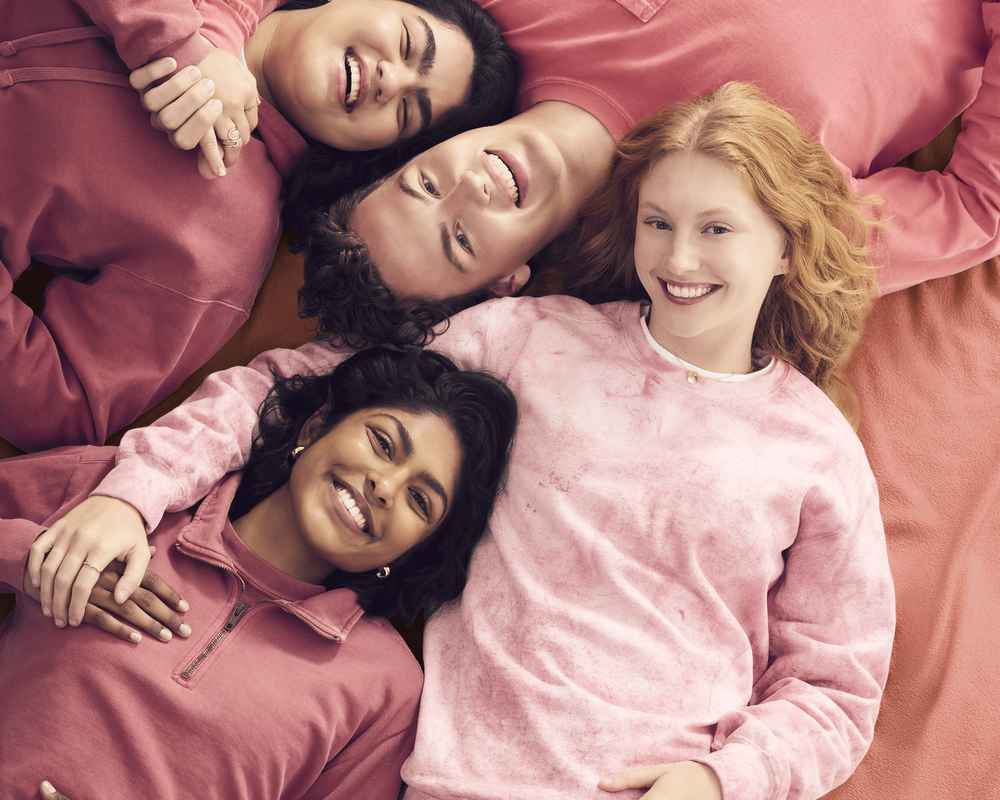 Deux femmes et deux hommes sont allongés et portent des pulls Comfort Colors roses en souriant.