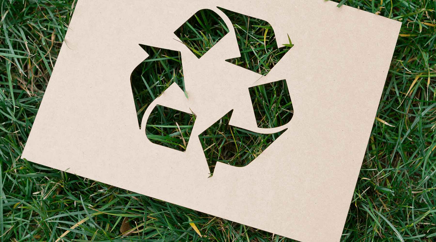 Un papel con una forma recortada del símbolo de reciclaje yace sobre la hierba.