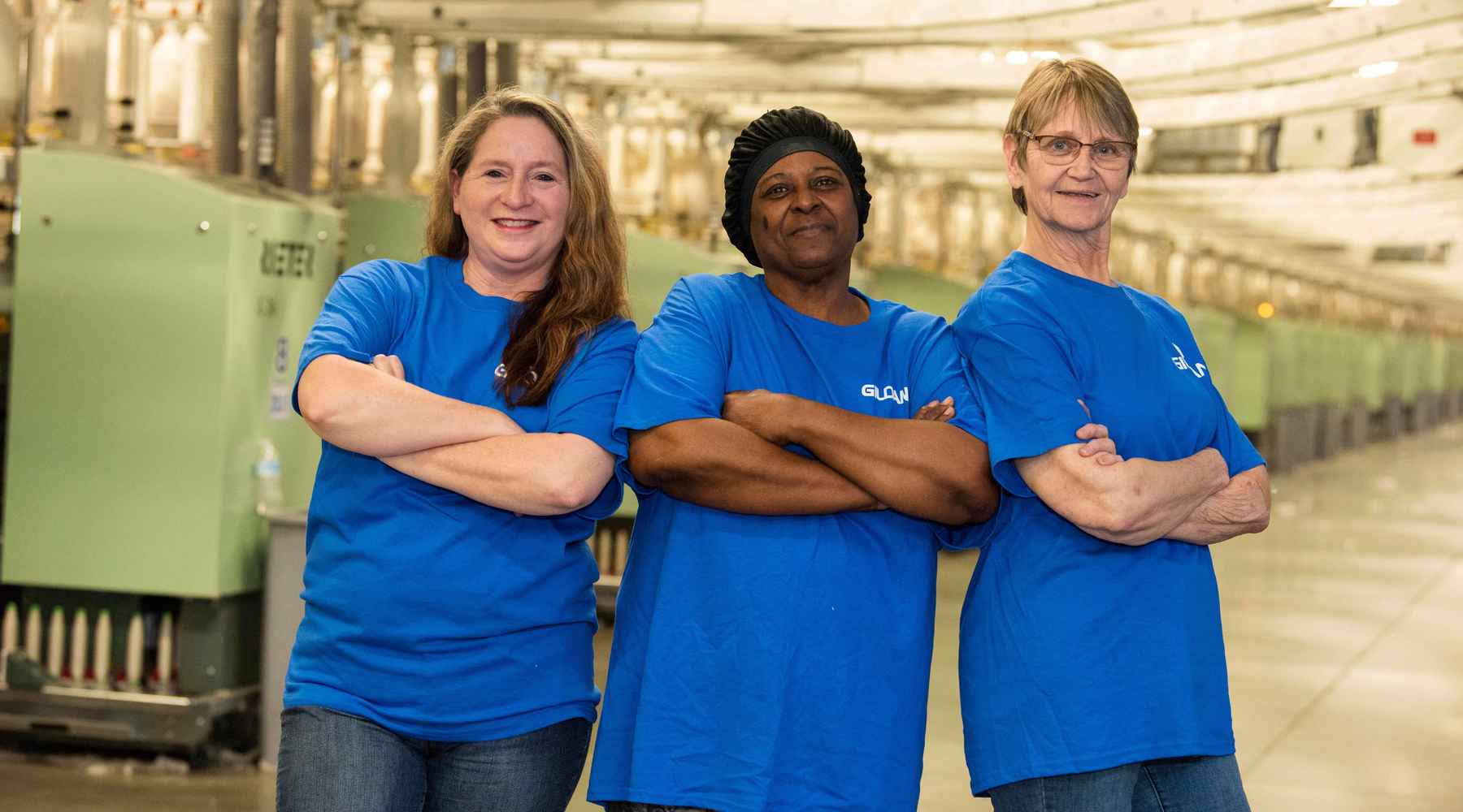 Trois employés de Gildan croisent les bras et sourient dans l'usine de filature.