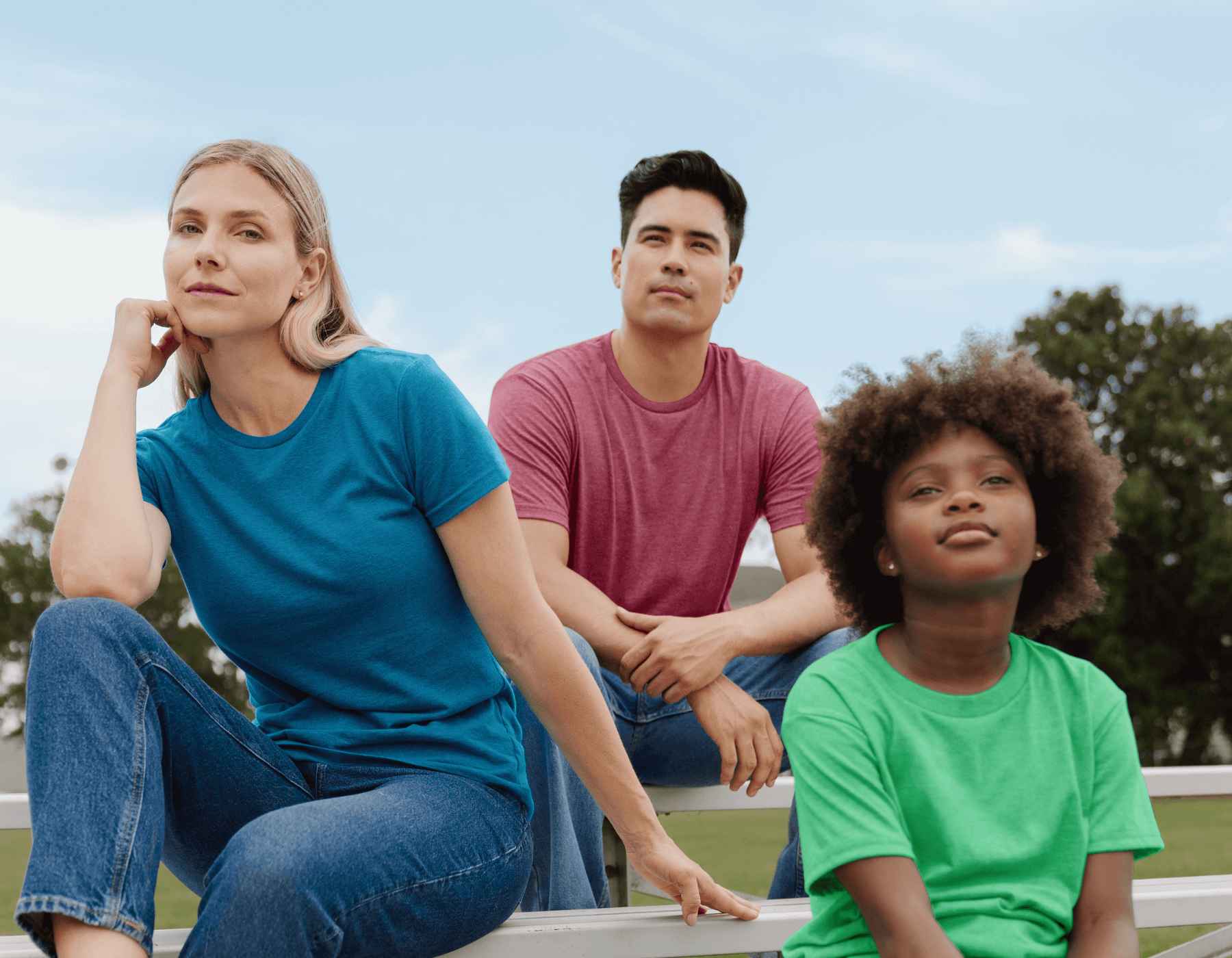 Une femme, un homme et un garçon portant des shirts Gildan sont assis à l'extérieur sur des gradins.